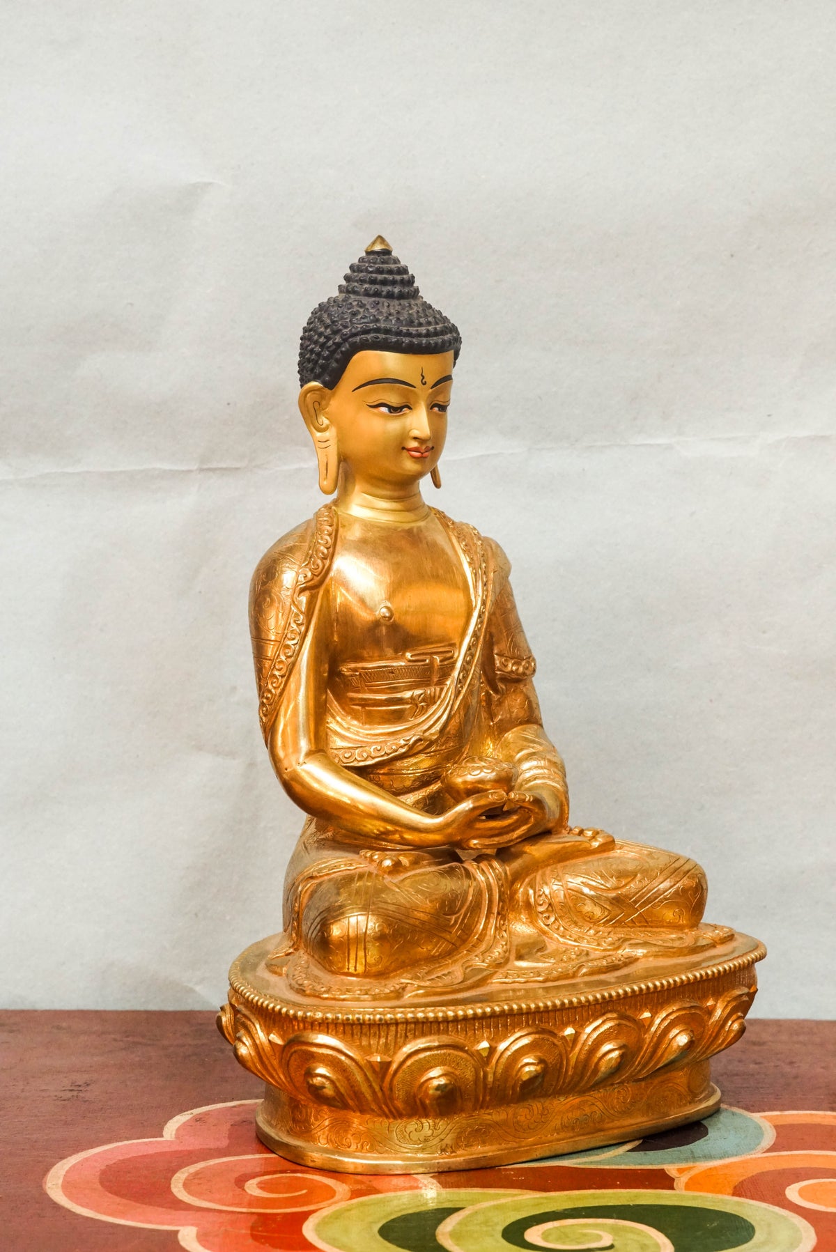 Shakyamuni Buddha Tibetan Buddhist gold-finished statue seated in full lotus posture on a lotus pedestal, with hands resting in meditation (dhyana mudra), wearing monastic robes, featuring elongated earlobes and ushnisha, symbolizing enlightenment, inner peace, and spiritual awakening.