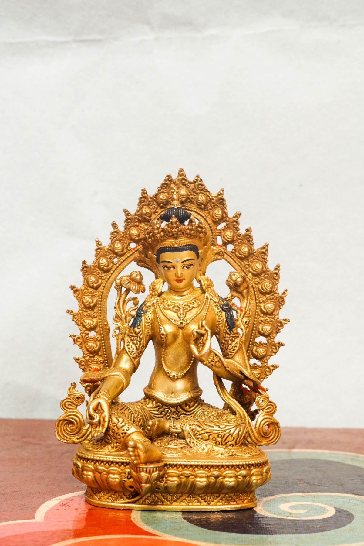 Gold-plated statue of Green Tara (Shyama Tara), the female Bodhisattva of compassion in Tibetan Buddhism, seated in royal ease posture on a lotus base within an ornate halo frame, wearing a five-leaf crown and jeweled ornaments, symbolizing swift protection and enlightened activity.