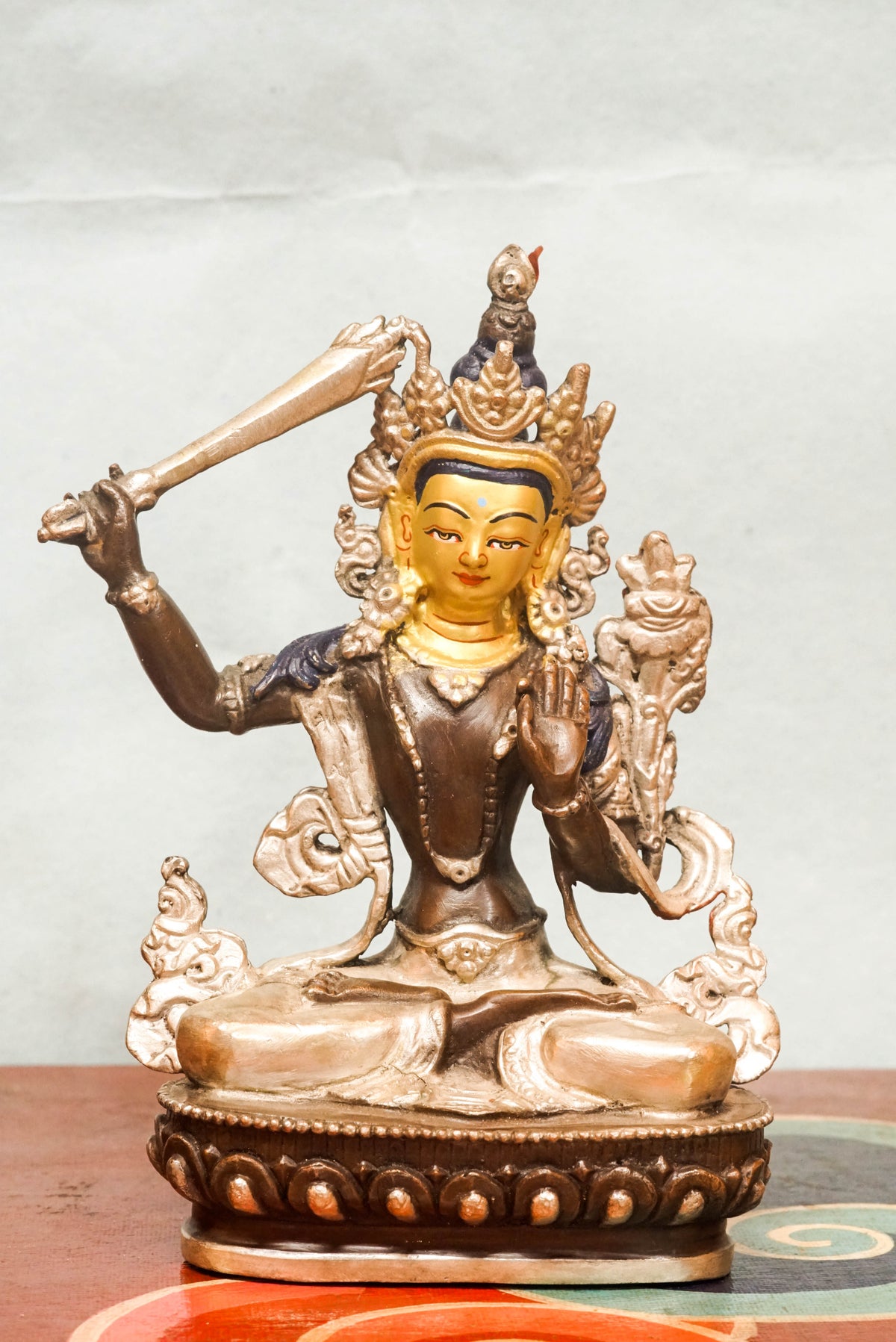 Gilt bronze statue of Manjushri, the Bodhisattva of Wisdom, seated in vajra posture on a lotus base, holding the flaming sword of transcendent wisdom in his raised right hand and the Prajñāpāramitā scripture on a lotus in his left, finely cast in traditional Himalayan Buddhist style.