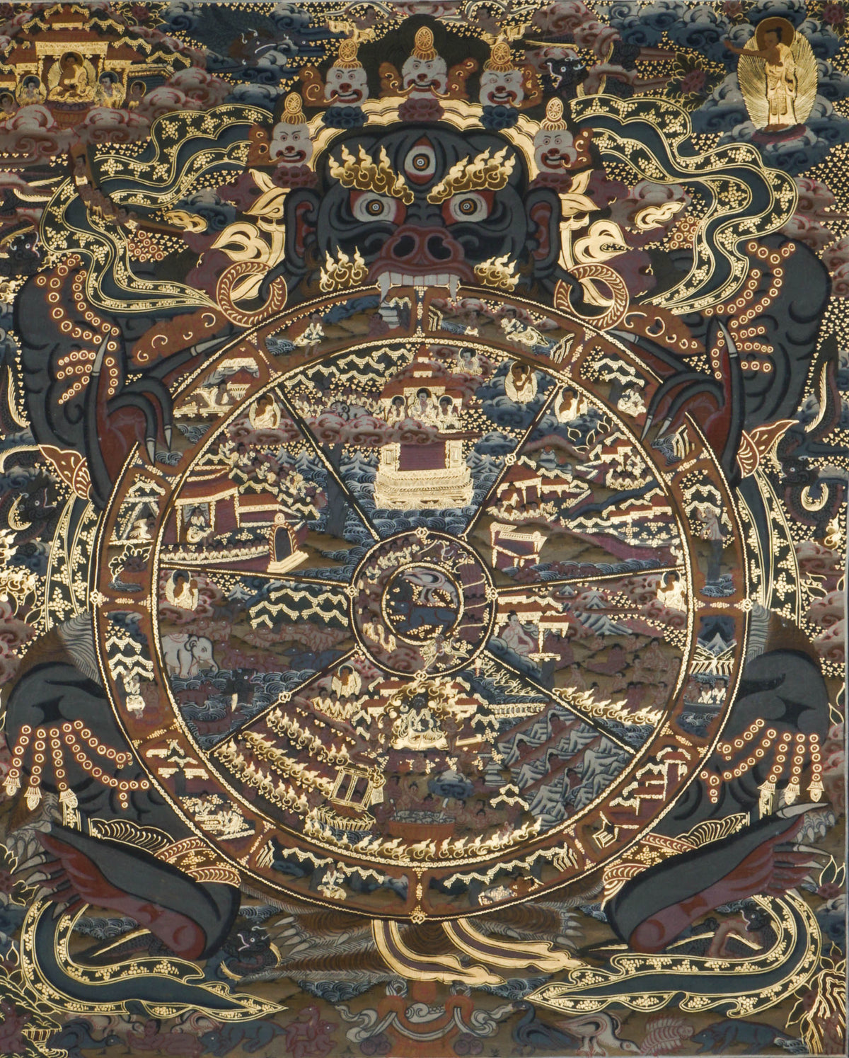 Detailed thangka-style painting showing a large circular wheel divided into multiple wedge-shaped sections filled with small human figures, buildings, animals, and landscape scenes, surrounded by concentric decorative rings. The wheel is held by a large dark blue multi-eyed figure with extended arms and clawed hands, set against a richly patterned background with clouds, flames, and ornate gold, brown, red, and blue detailing.