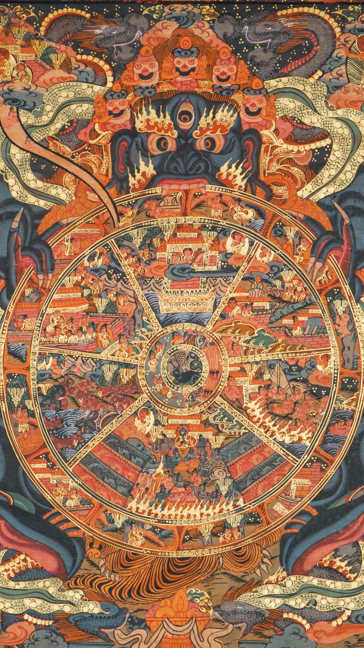 Detailed thangka painting showing a large circular wheel divided into multiple segments, each filled with small human figures, animals, buildings, and landscape scenes, held by a large blue figure with multiple eyes and arms, surrounded by clouds, flames, and dense decorative patterns within a rectangular border.