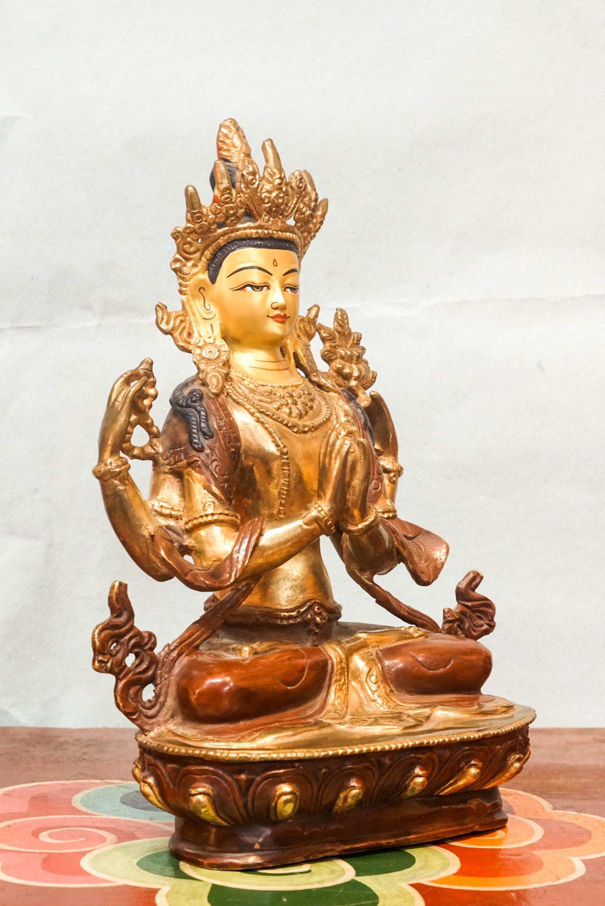 Four-armed Chenrezig (Avalokiteshvara), the Bodhisattva of Compassion, Tibetan Buddhist bronze statue seated in full lotus posture on a lotus pedestal, with two hands joined in prayer (anjali mudra) holding a wish-fulfilling jewel, and two outer hands holding a crystal mala and lotus flower, adorned with a five-leaf crown and bodhisattva ornaments, symbolizing infinite compassion and enlightened activity.