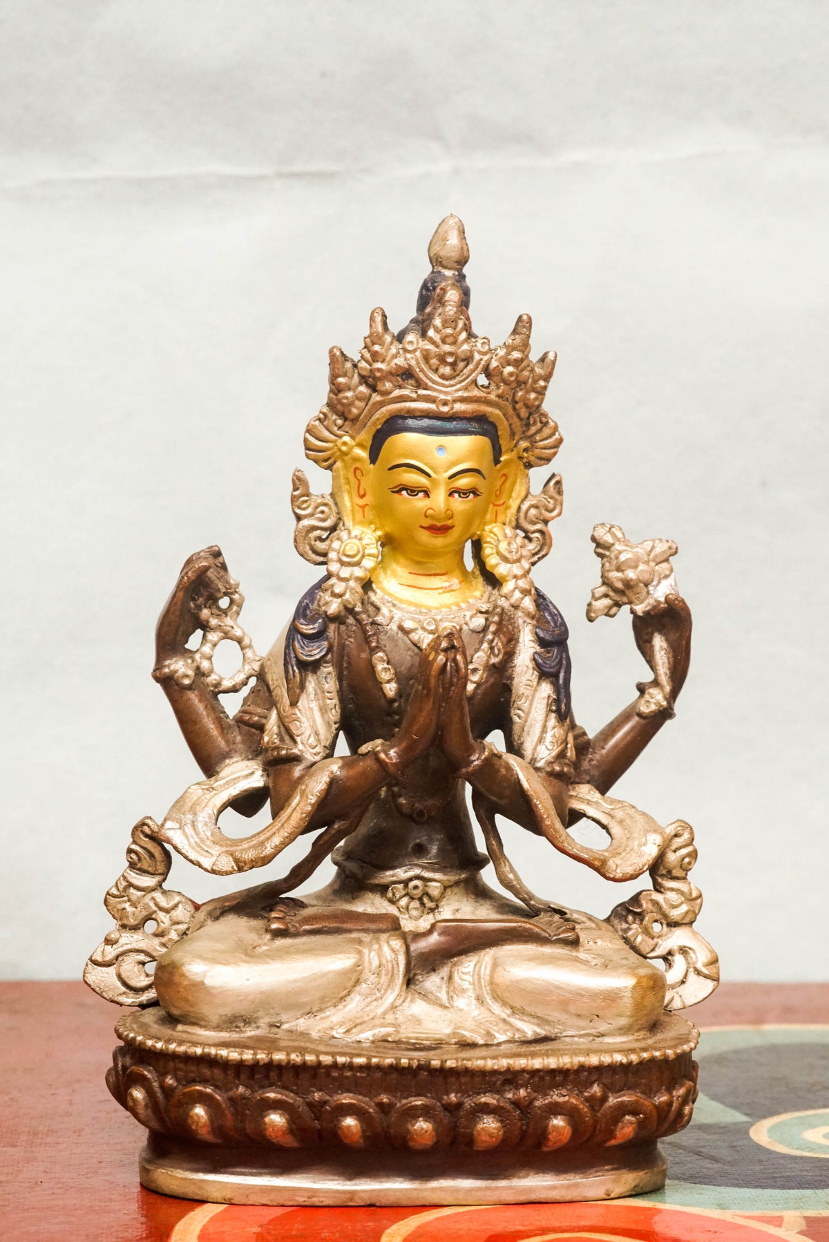 Chenrezig (Avalokiteshvara), the Bodhisattva of Compassion, bronze Tibetan Buddhist statue seated in full lotus posture on a lotus pedestal, with hands joined in prayer (anjali mudra) holding a wish-fulfilling jewel, adorned with a five-leaf crown, jeweled ornaments, and serene expression, symbolizing infinite compassion and spiritual guidance.