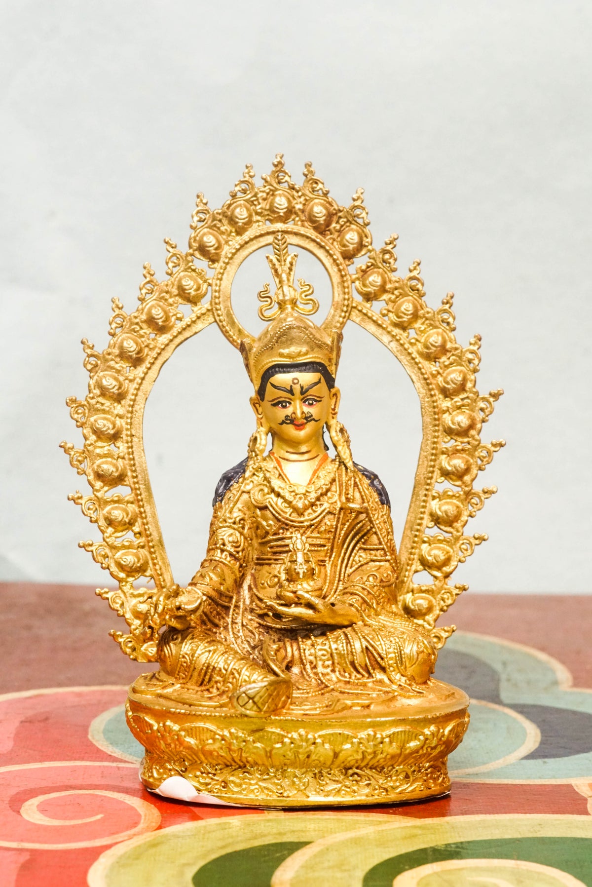 Gilt bronze statue of Guru Rinpoche (Padmasambhava), the Lotus-Born master of Tibetan Buddhism, seated in royal ease posture on a lotus base, wearing a lotus crown and monastic robes, with ornate halo and traditional Himalayan Buddhist craftsmanship.
