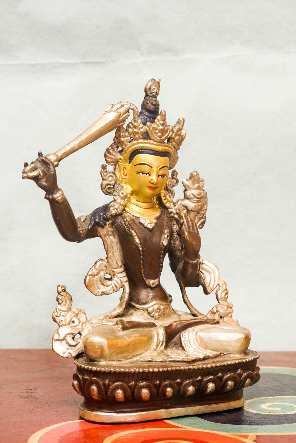 Gilt bronze statue of Manjushri, the Bodhisattva of Wisdom, seated in vajra posture on a lotus base, holding the flaming sword of transcendent wisdom in his raised right hand and the Prajñāpāramitā scripture on a lotus in his left, finely cast in traditional Himalayan Buddhist style.