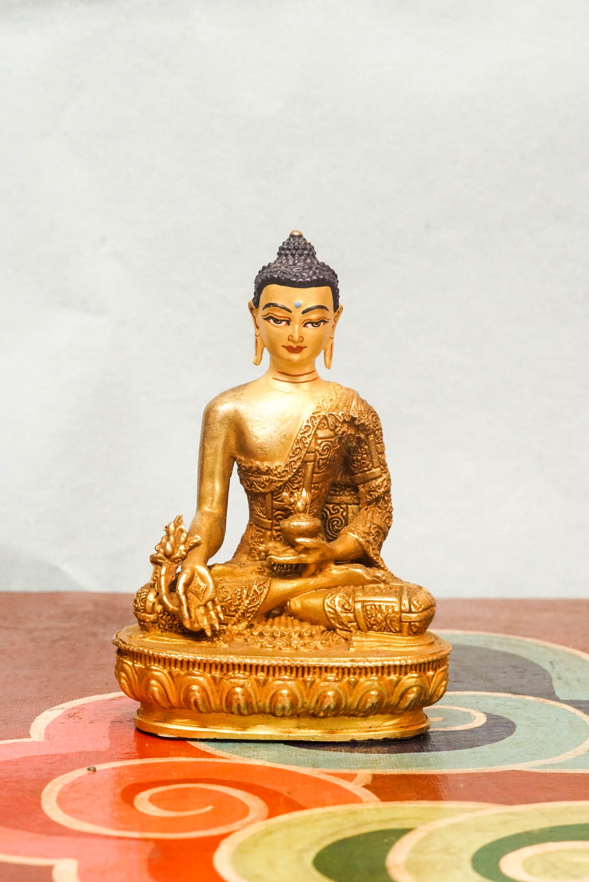Handcrafted Medicine Buddha statue with fully opened eyes, holding a healing bowl, surrounded by a radiant lapis aura, seated on a lotus pedestal.