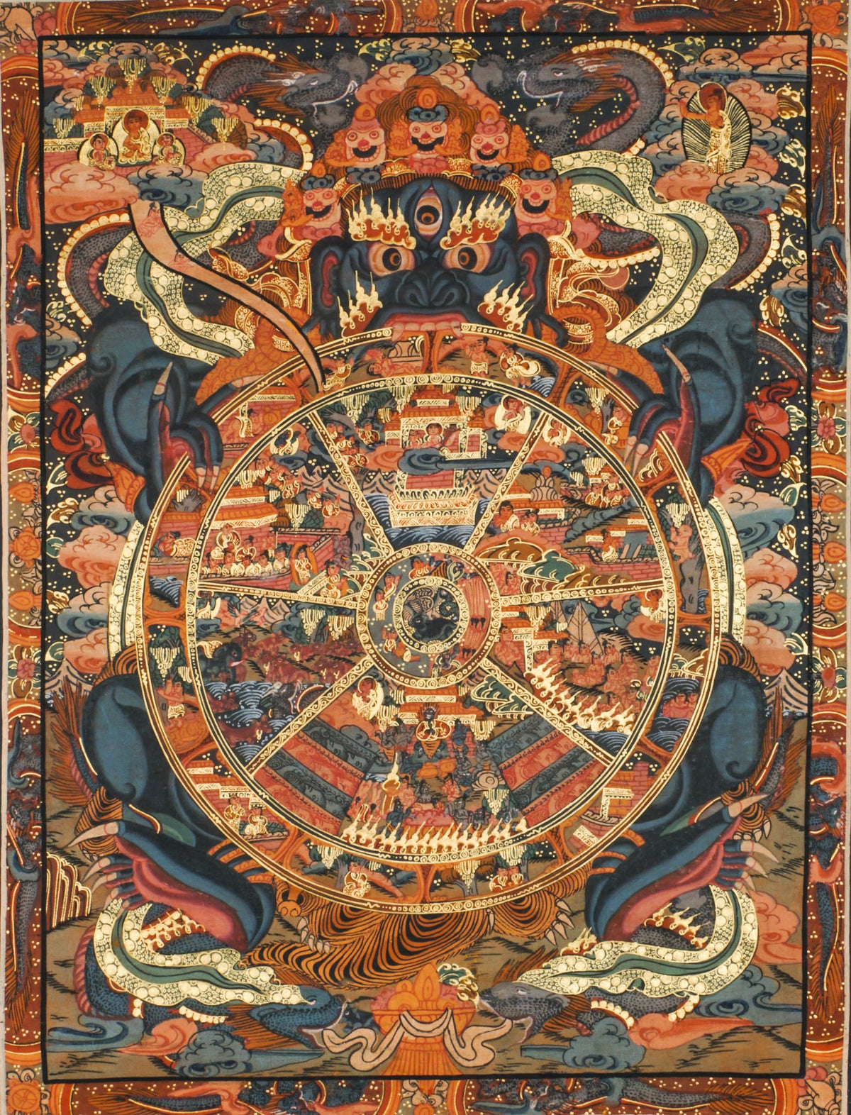 Detailed thangka painting showing a large circular wheel divided into multiple segments, each filled with small human figures, animals, buildings, and landscape scenes, held by a large blue figure with multiple eyes and arms, surrounded by clouds, flames, and dense decorative patterns within a rectangular border.
